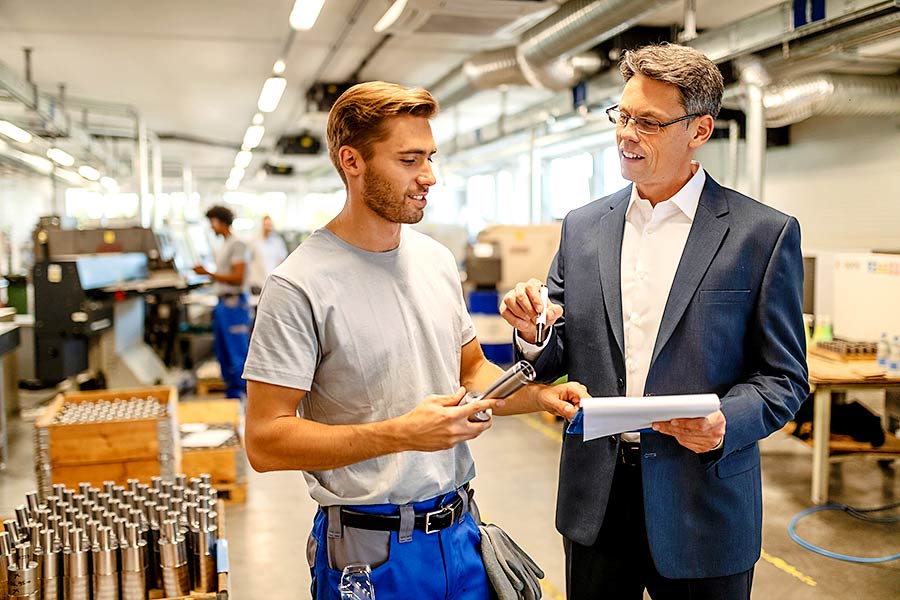 Interner Unternehmensverkauf: Unternehmer und Führungskraft im Gespräch in einer Fabrikhalle.